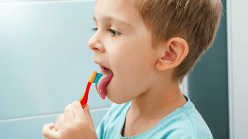 A child cleaning their tongue with a toothbrush.